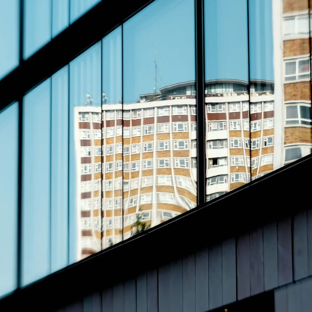 Glass facade reflecting a high-rise under blue sky — Lookout