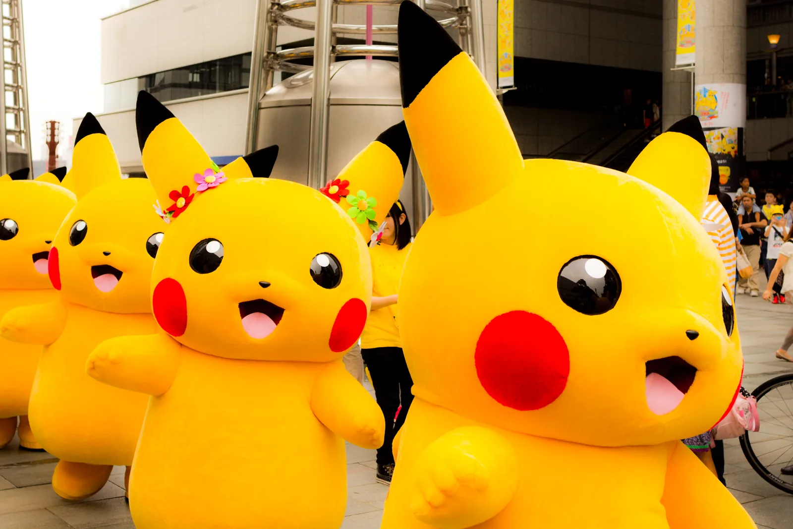 Pikachu mascots in a Yokohama street parade, yellow costumes with black-tipped ears, one wearing a flower crown.
