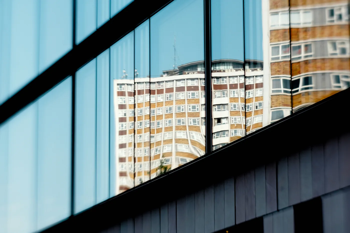 Glass facade reflecting a high-rise under blue sky — Lookout