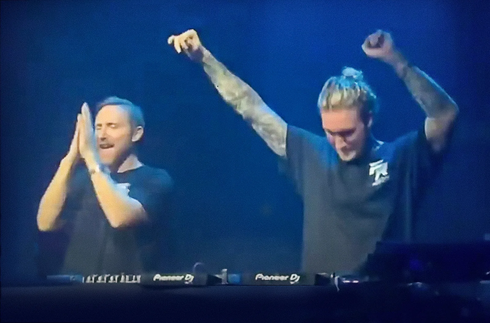 David Guetta and MORTEN behind a pair of Pioneer decks at Hï Ibiza in 2022. Guetta is clapping. MORTEN has both arms in the air under blue light.